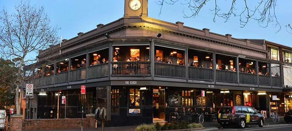 The Clock Hotel at dusk, its wraparound corner balcony full of drinkers beneath the clock tower