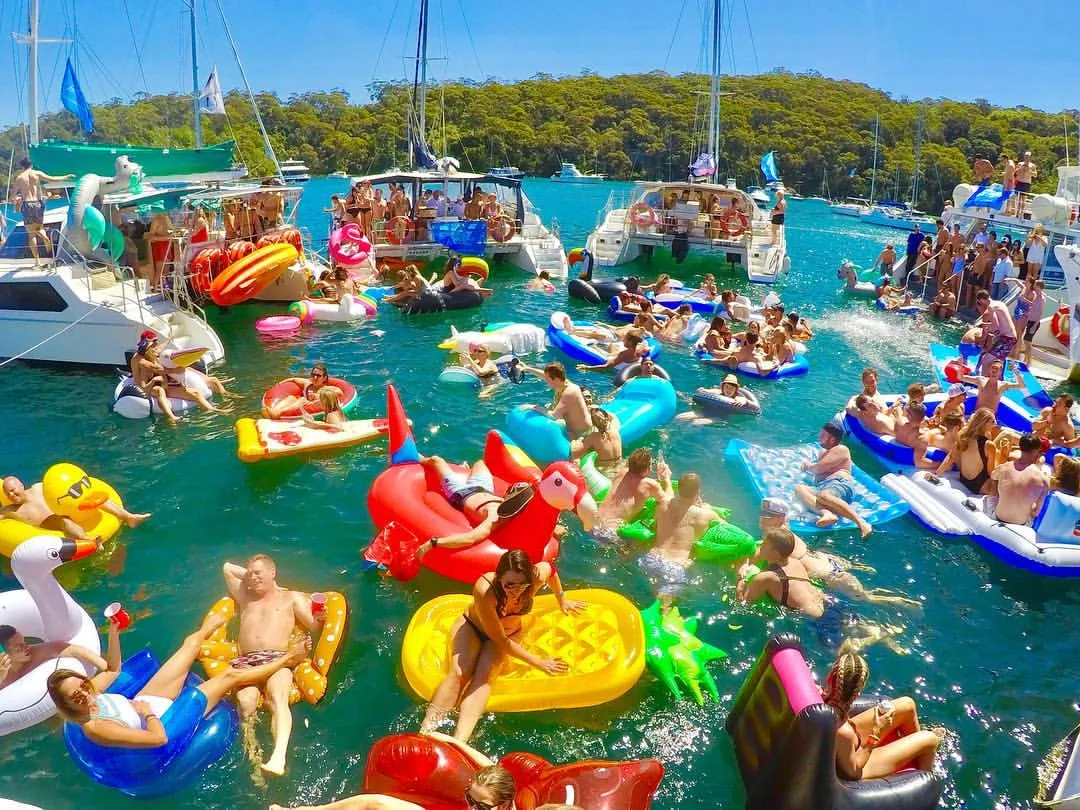 Crowd floating on inflatables in the water between boats at The Yacht Social Club raft-up, Sydney Harbour