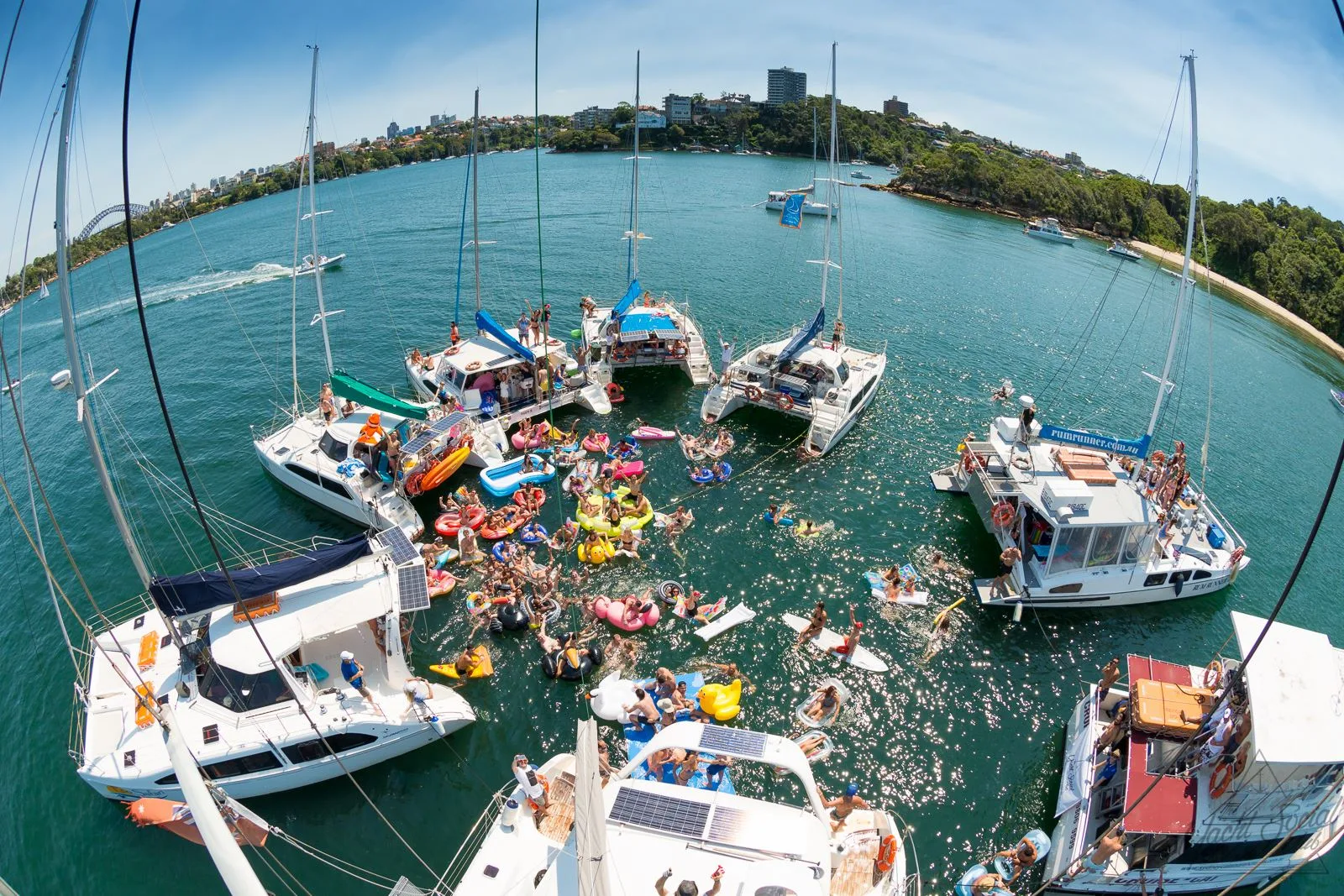 Aerial view of the raft-up at The Yacht Social Club, catamarans moored together in Sydney Harbour with swimmers and inflatables between them