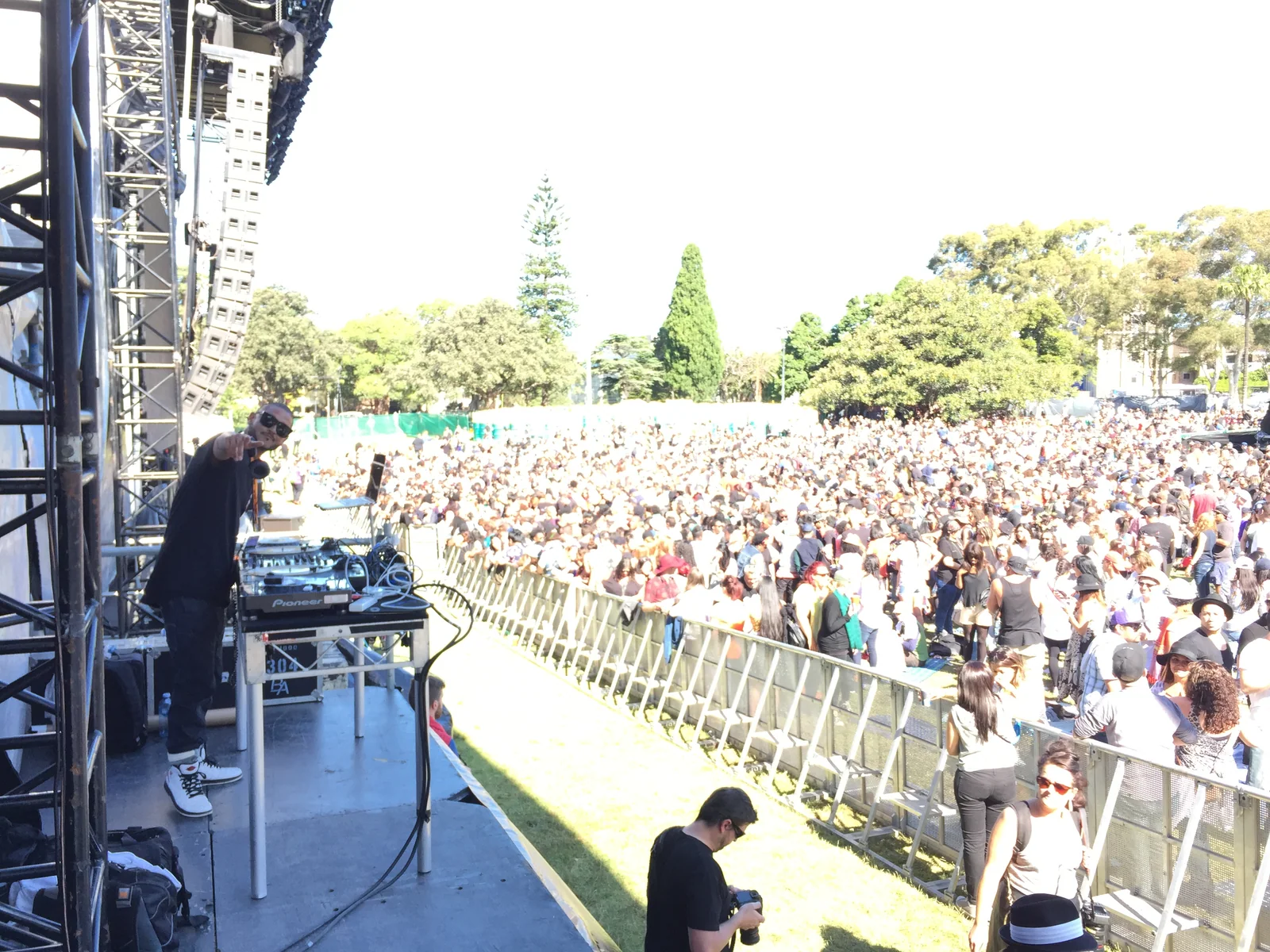 CMAN pointing to the camera from behind the decks on the Soulfest stage, the daytime Victoria Park crowd stretching out below